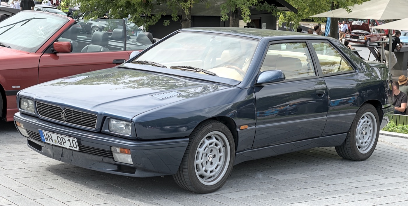 Dark blue 1990s Maserati Ghibli II coupé with a square-cut body and four headlamps, parked at a car meeting