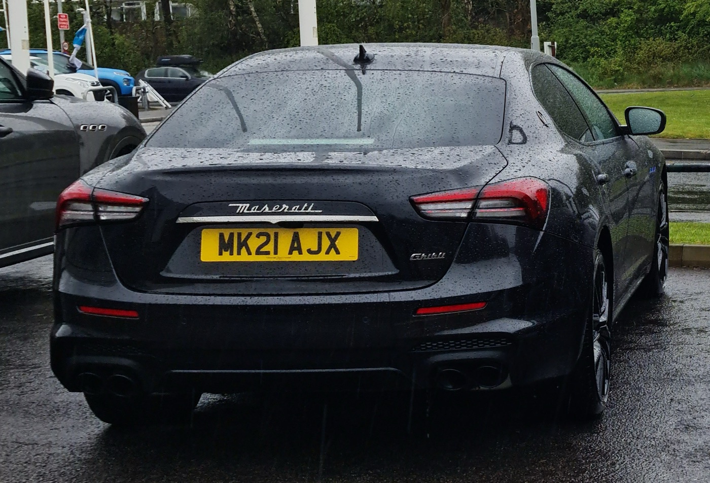 Black 2021 Maserati Ghibli saloon seen from behind in the rain, with boomerang-shaped tail lights and a UK number plate