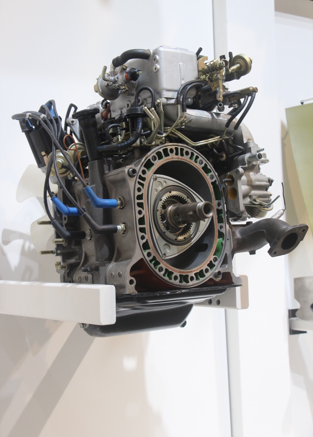 Cutaway Mazda 13B twin-rotor engine on a museum stand, showing a three-sided rotor inside its oval housing