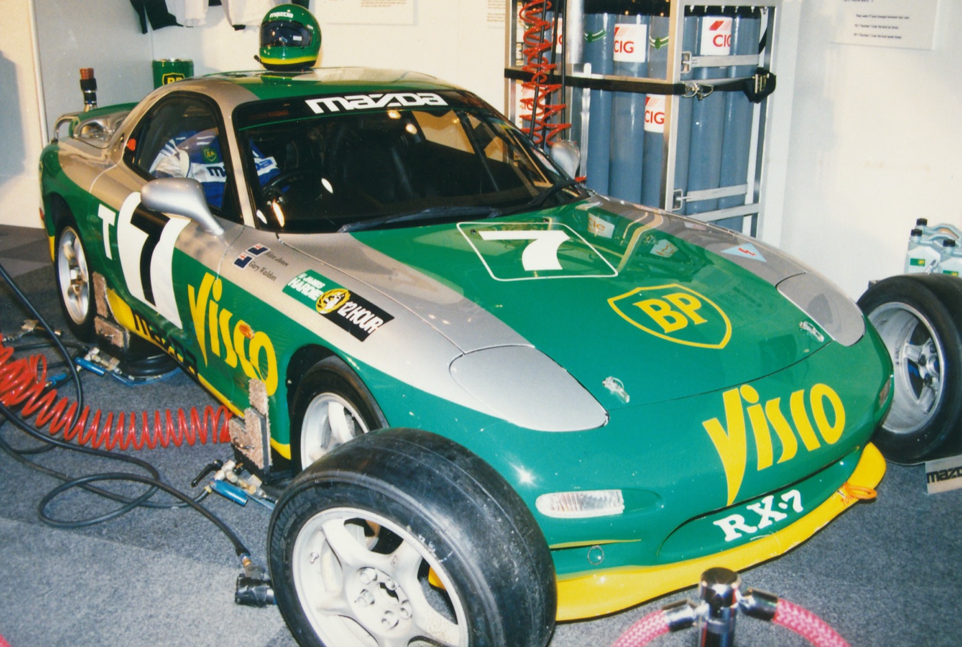 Green and silver Mazda RX-7 FD race car numbered 7 in BP and Visco colours, in a pit garage with its bonnet down