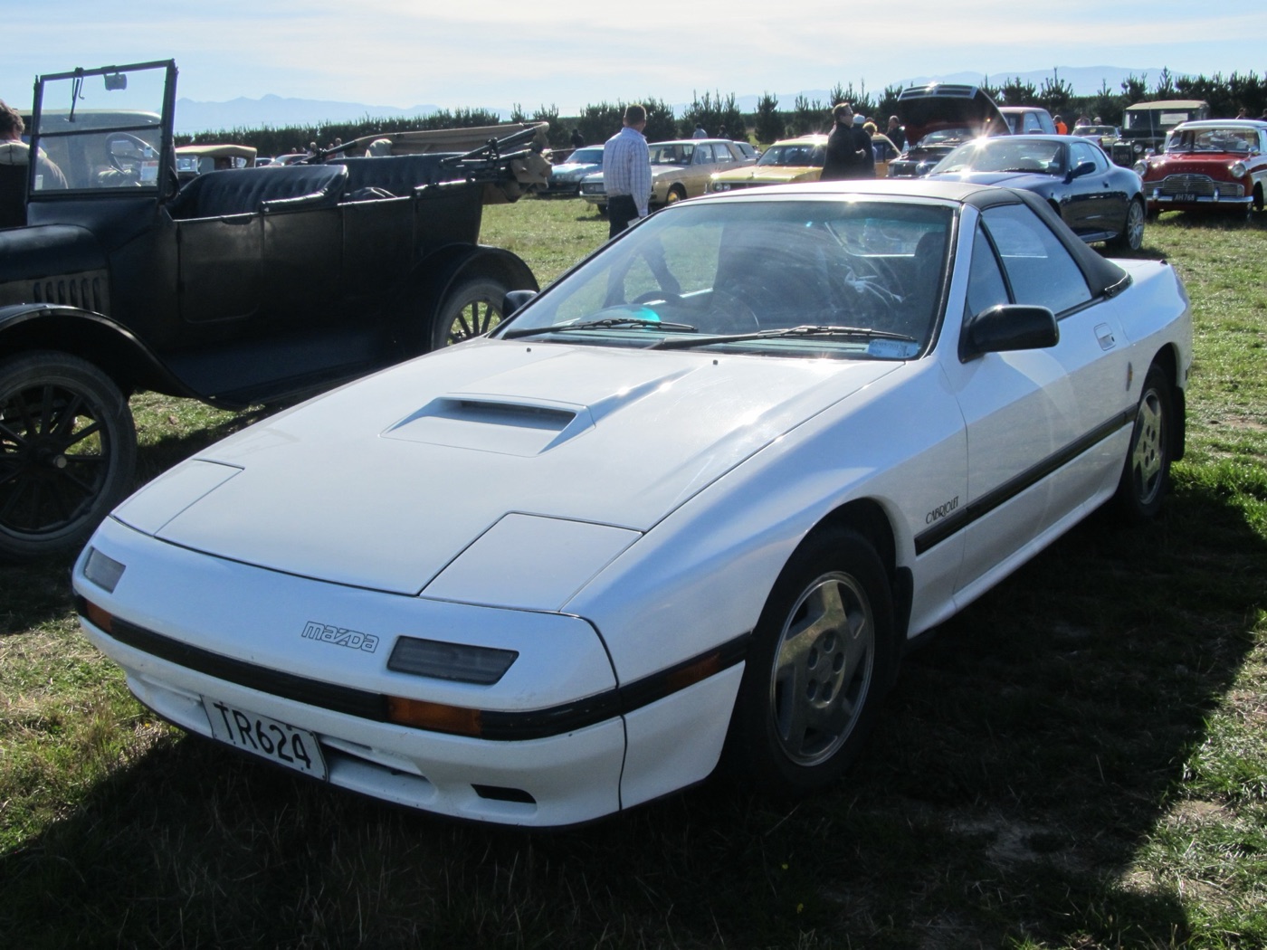 White Mazda RX-7 FC Cabriolet with its roof up, parked on grass at a car show beside an open vintage car