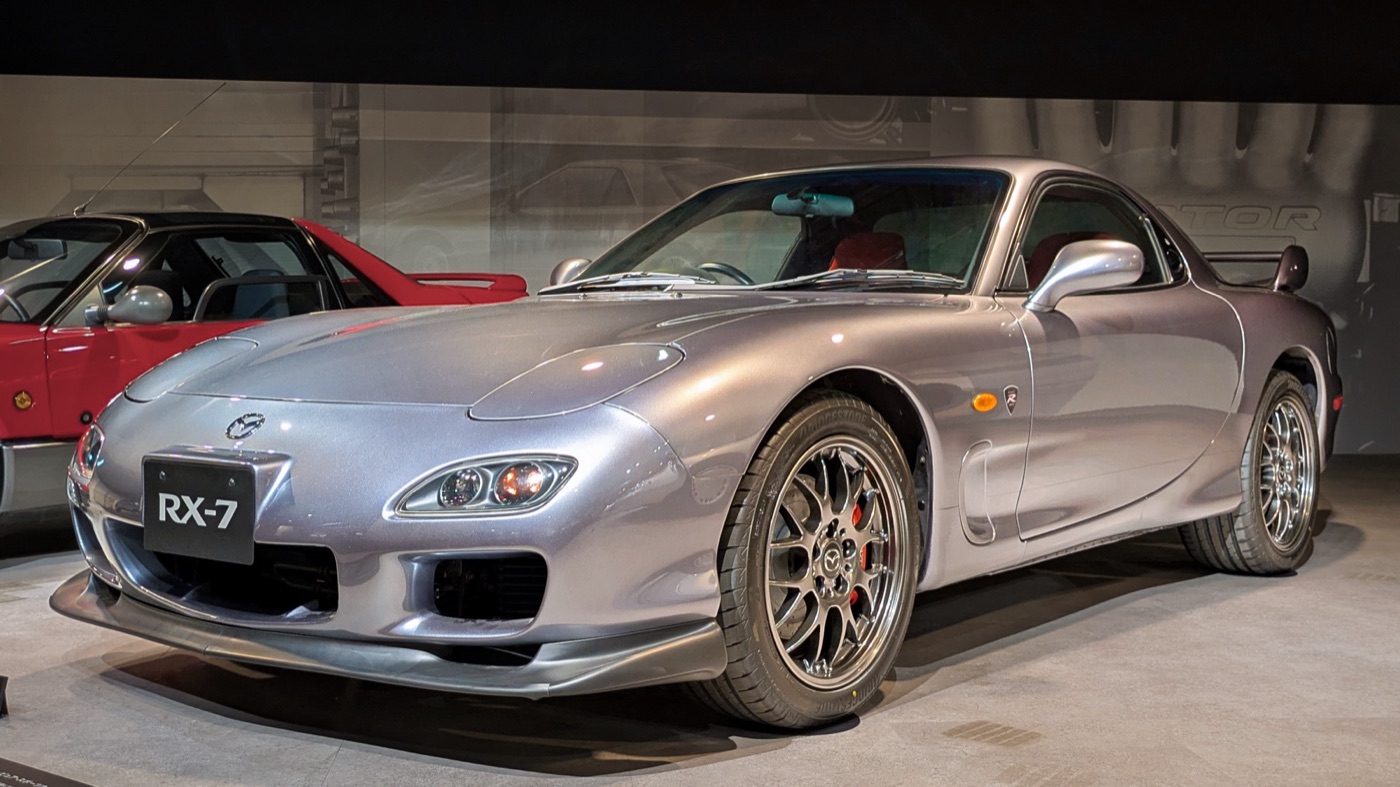 Silver Mazda RX-7 Spirit R Type A with gold-grey BBS wheels and red brake calipers in a museum hall