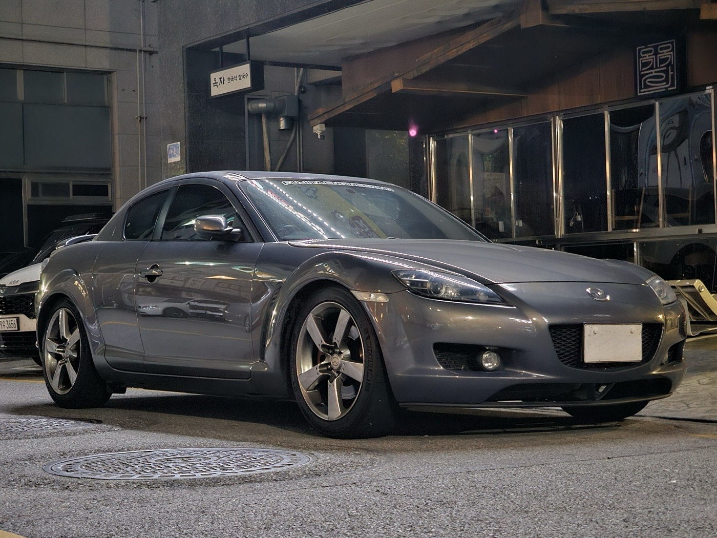 Grey Mazda RX-8 four-door coupé parked on a city street at dusk