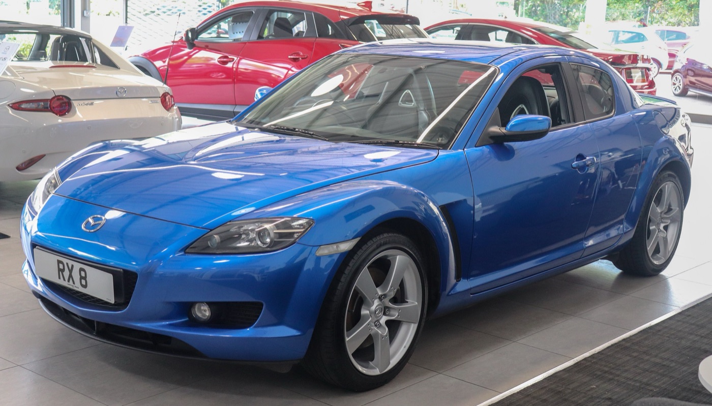 Blue first-generation Mazda RX-8 with five-spoke silver wheels and an RX 8 number plate in a showroom