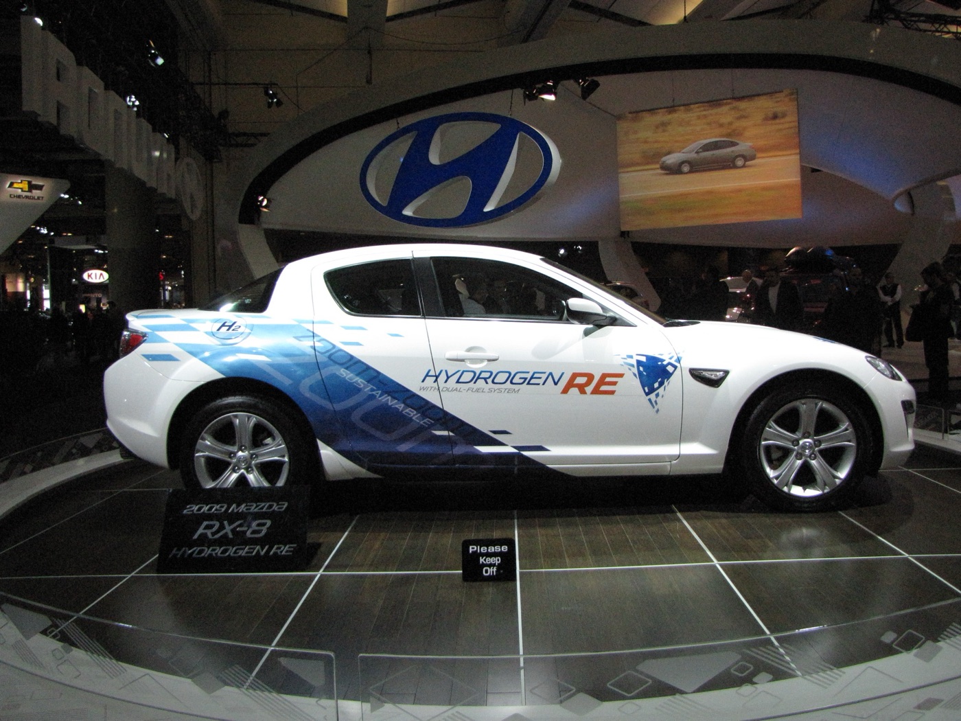 White Mazda RX-8 Hydrogen RE in blue and white livery with Hydrogen RE lettering on the door, on a motor show stand