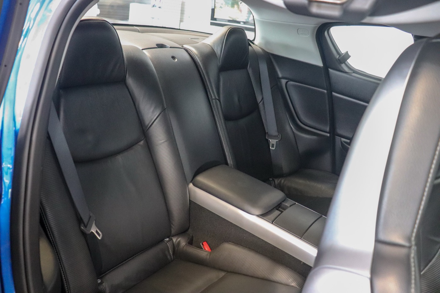 Two black leather rear seats of a Mazda RX-8 divided by a centre console and armrest, seen through the open rear door