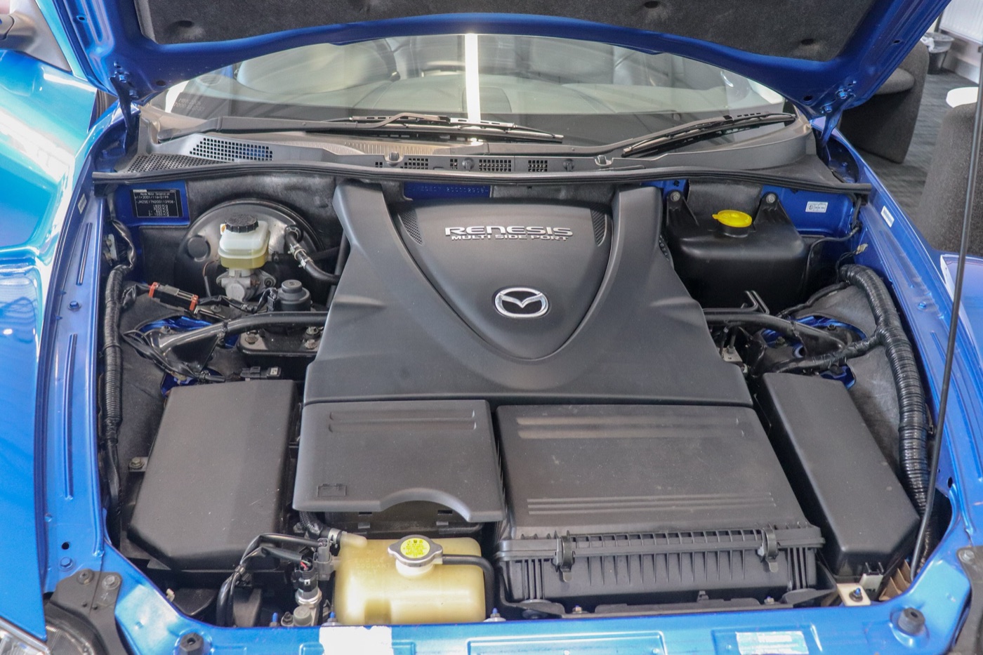 Engine bay of a blue Mazda RX-8 with a black engine cover marked RENESIS Multi Side Port, set low and far back