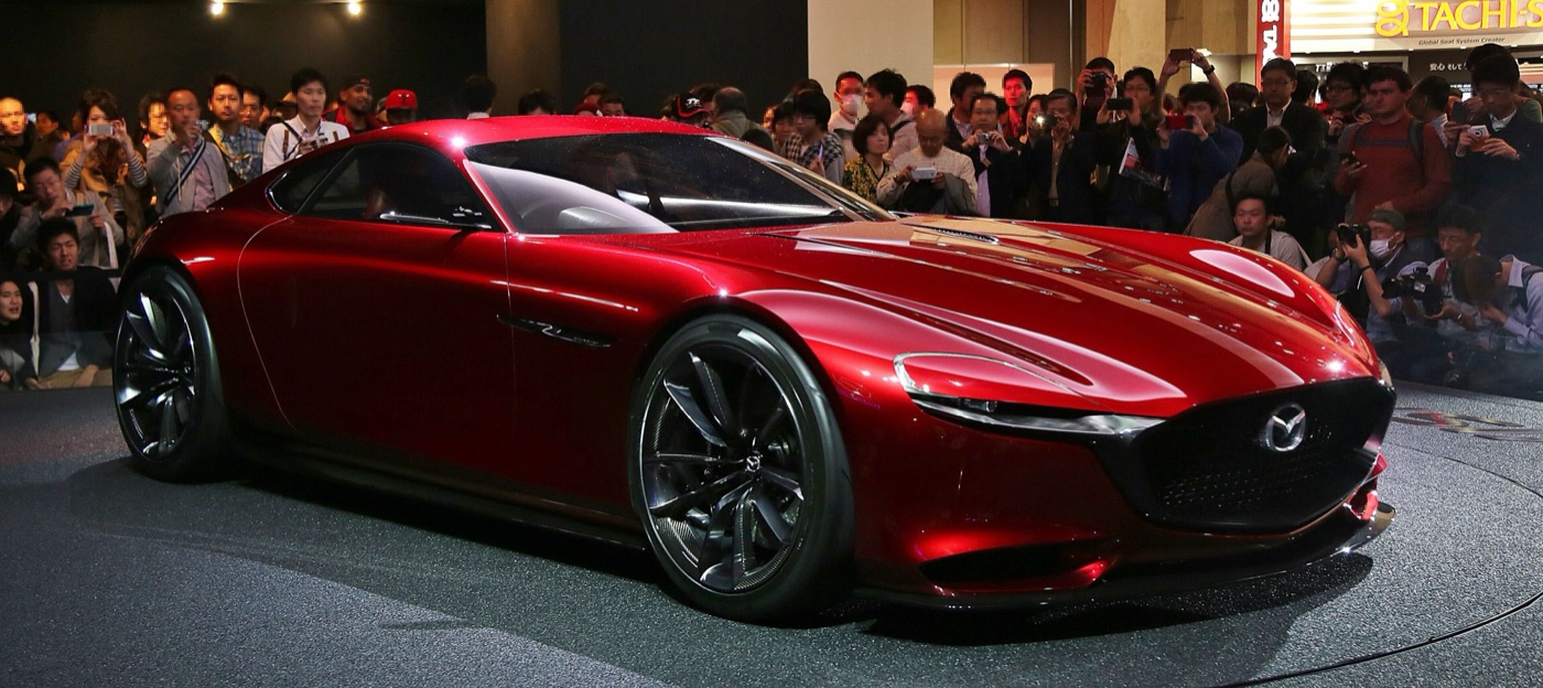 Red Mazda RX-Vision concept coupe with a long bonnet on a motor show stand, with visitors photographing it behind