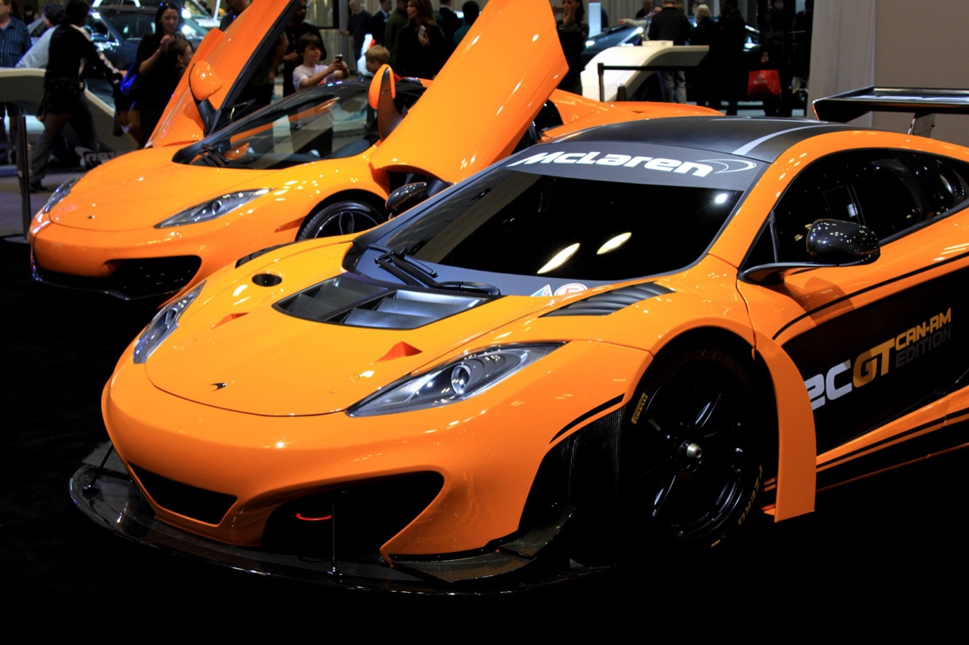 Orange McLaren 12C GT Can-Am Edition with a carbon splitter and rear wing in front of an orange 12C with its doors open