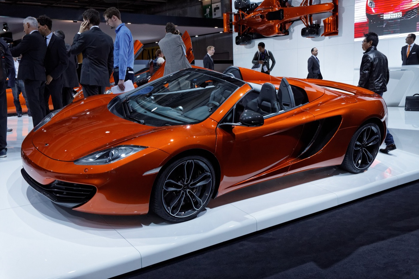 Orange McLaren 12C Spider with its roof folded on a white stand at a motor show