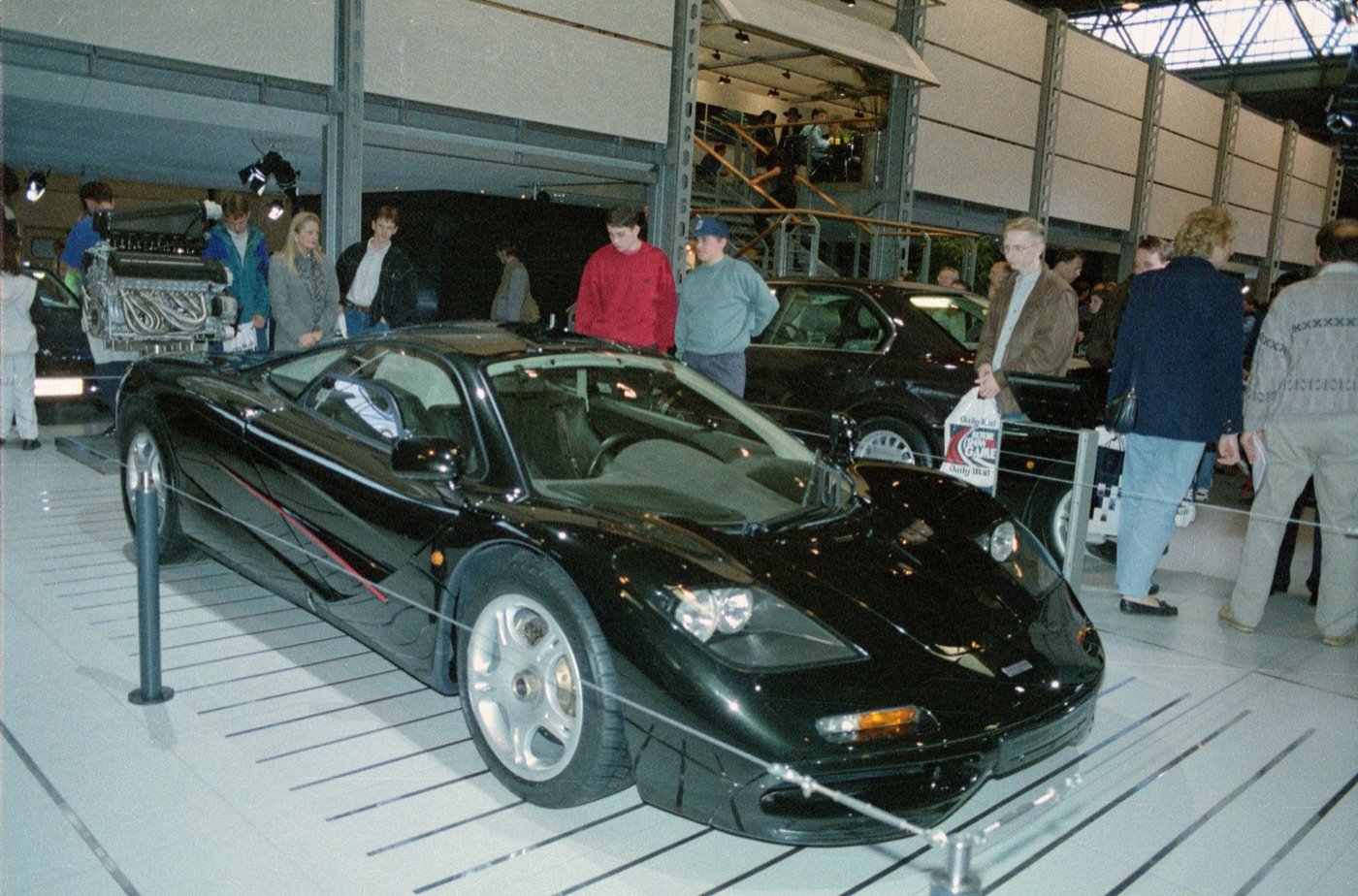 Black McLaren F1 on a show stand, with its BMW V12 engine displayed on a plinth behind
