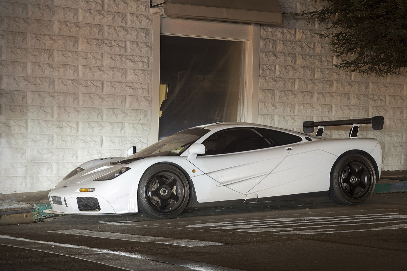 White McLaren F1 with a fixed rear wing and black five-spoke wheels parked on a street at night