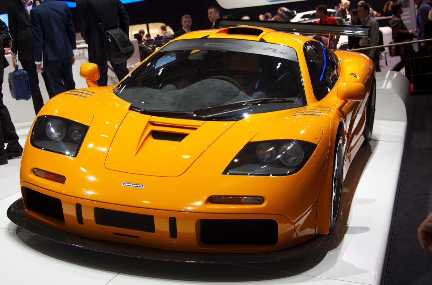Orange McLaren F1 LM with a fixed rear wing on a motor show stand