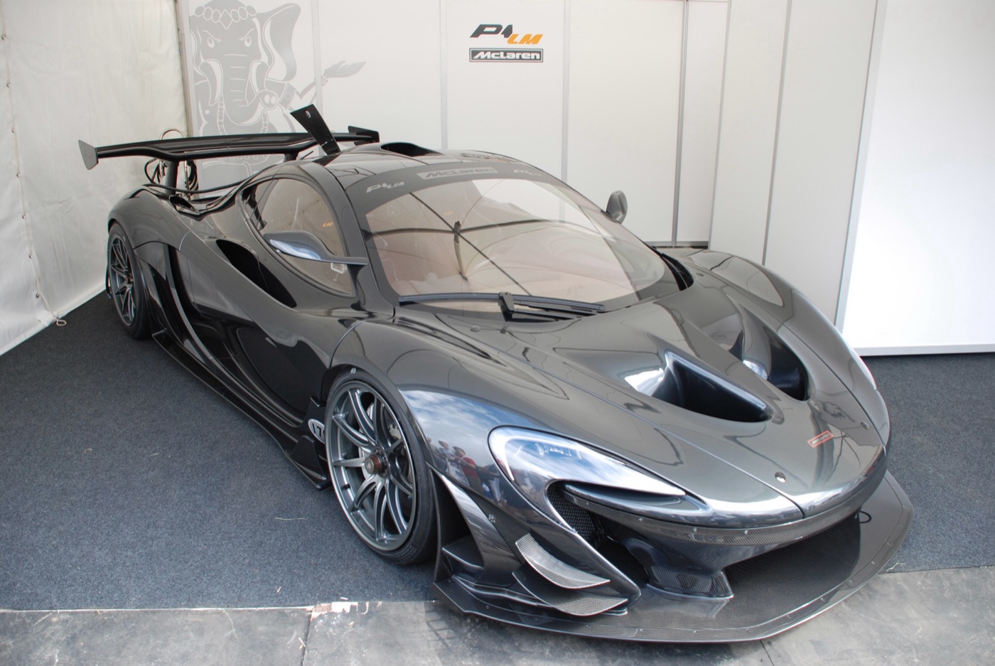 Dark grey McLaren P1 LM with a tall rear wing and front dive planes in a white display tent