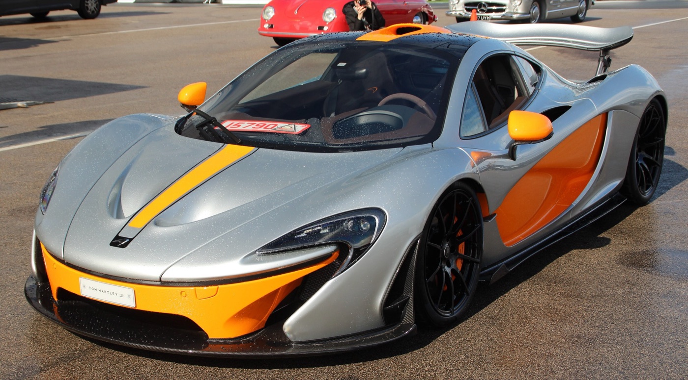 Silver McLaren P1 with an orange bonnet stripe, orange lower body and orange mirrors on a circuit paddock
