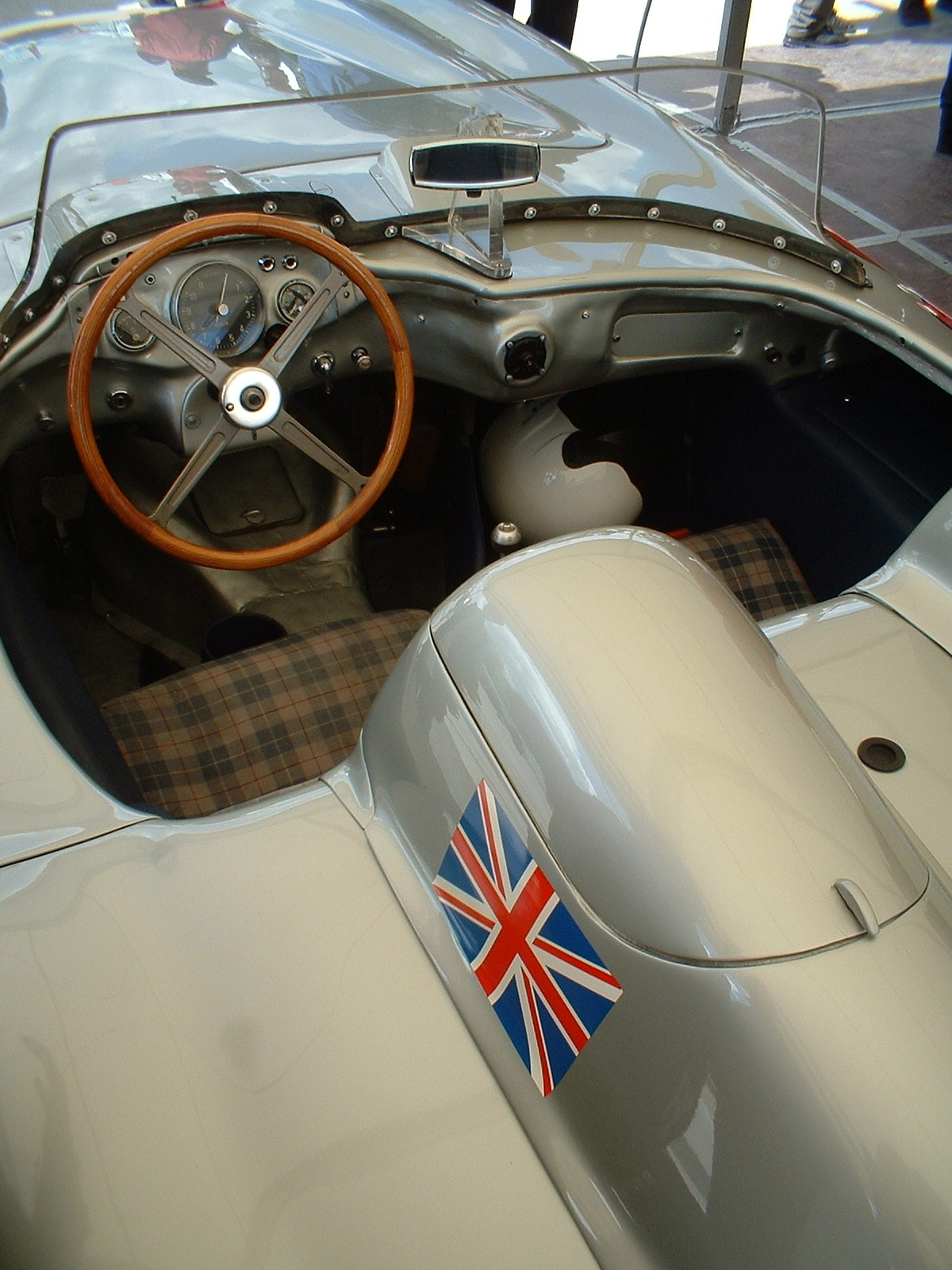Cockpit of a Mercedes-Benz 300 SLR with a wood-rimmed steering wheel, tartan seats, a helmet on the passenger side and a Union Jack on the bodywork
