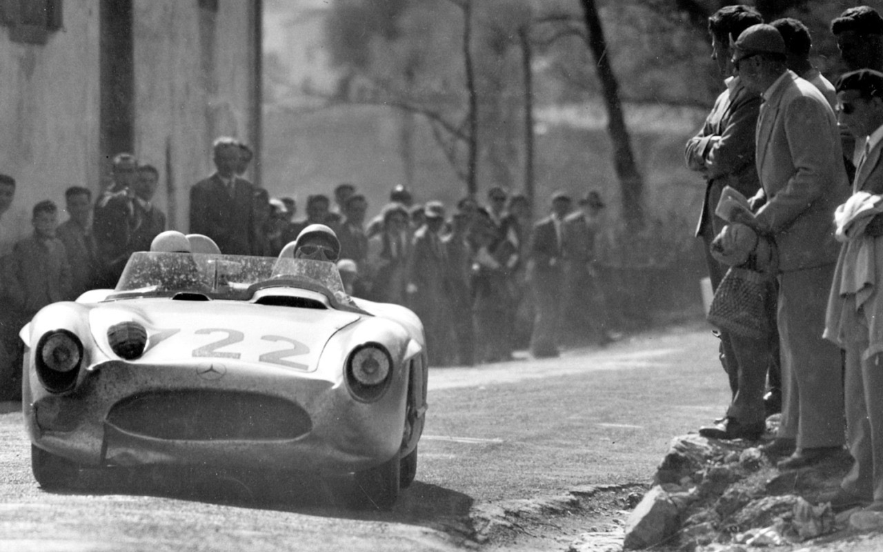 Black and white photo of the dusty Mercedes-Benz 300 SLR number 722 with Moss and Jenkinson aboard, passing spectators on a village road