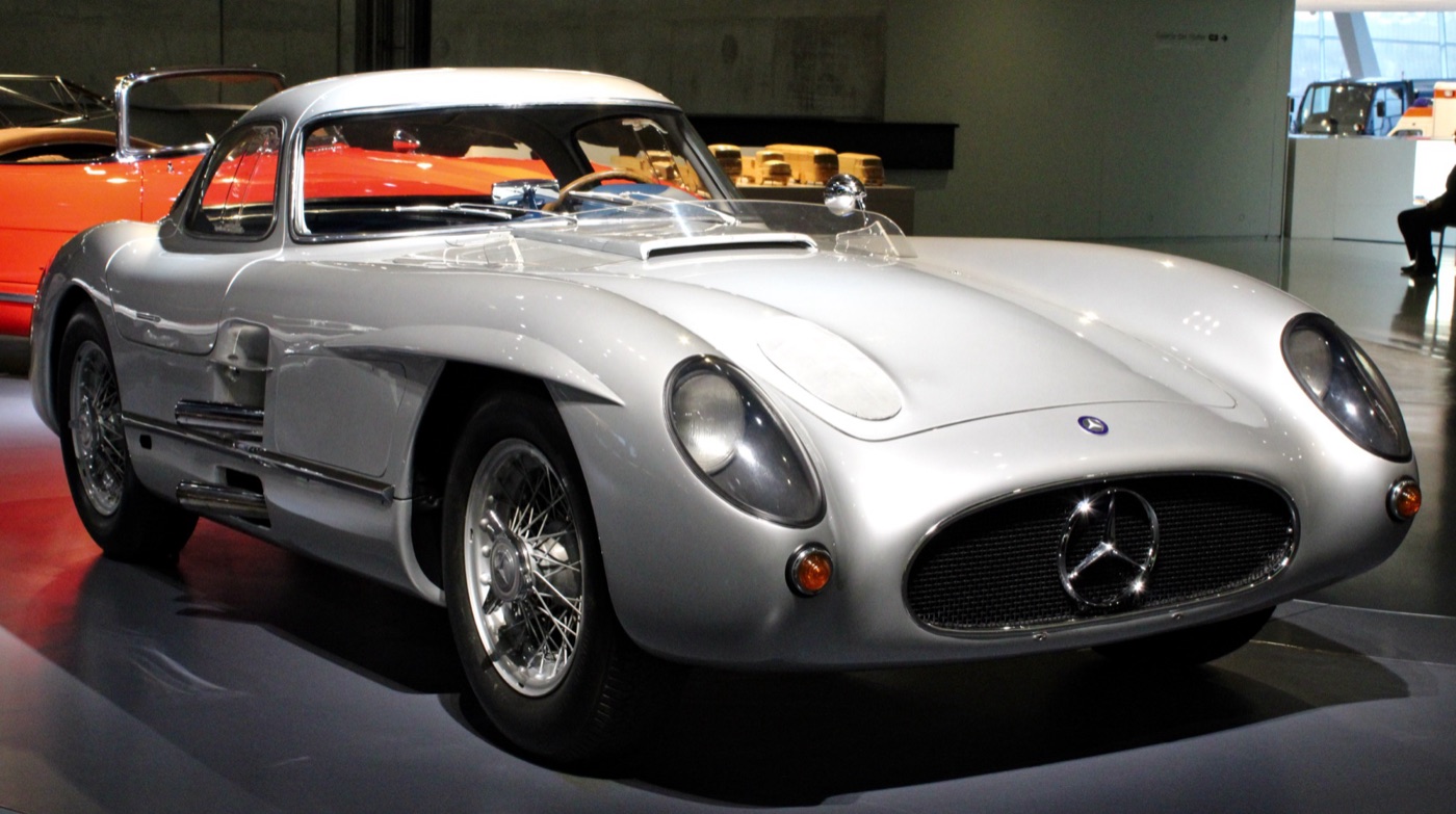 Silver Mercedes-Benz 300 SLR Uhlenhaut Coupé in a museum hall, front three-quarter view with gull-wing roof and wire wheels