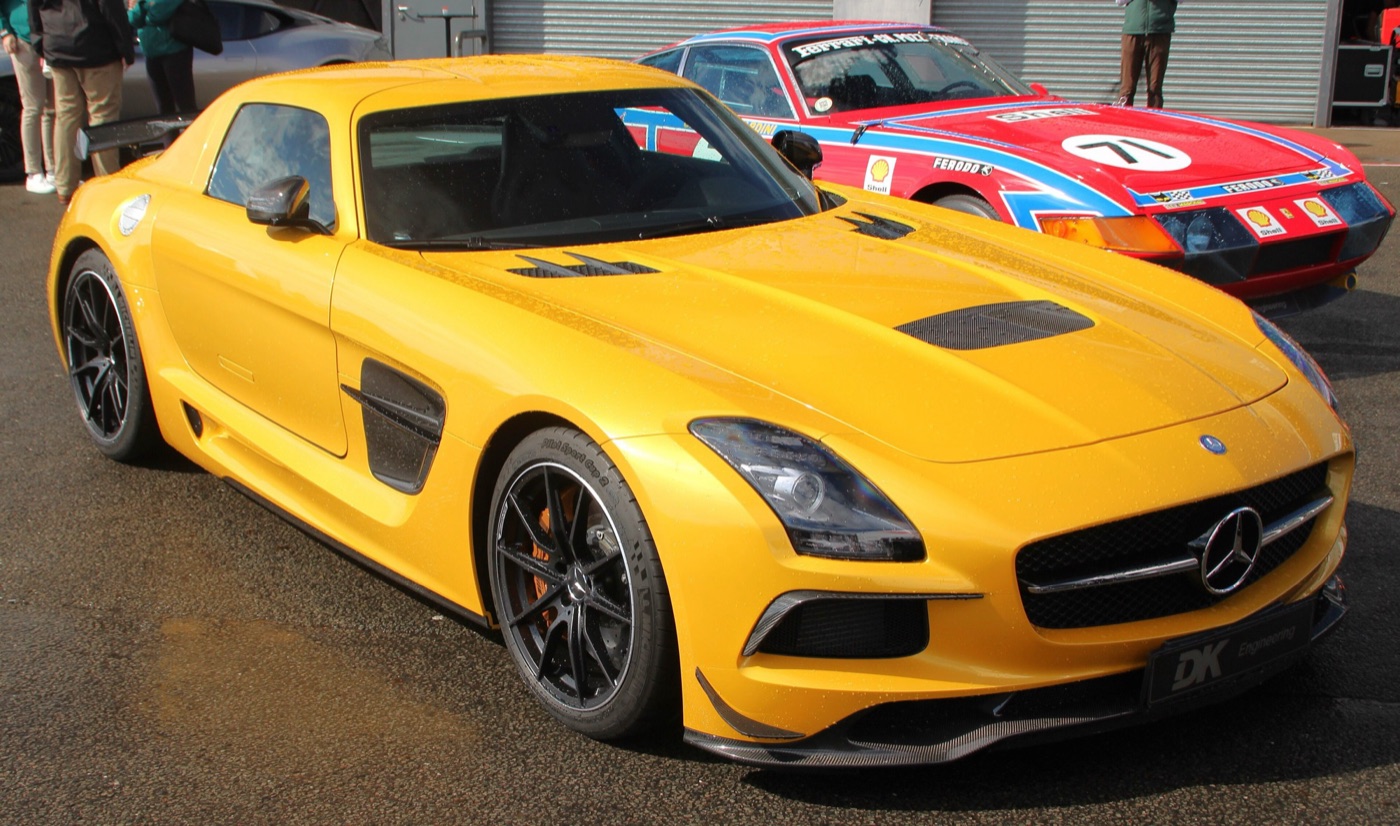 Yellow SLS AMG Black Series with black wheels, carbon front splitter and bonnet vent parked in a paddock