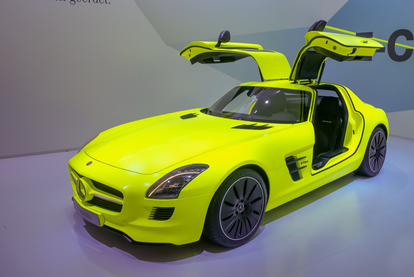 Fluorescent yellow-green SLS AMG E-Cell prototype with its gullwing doors raised on a white show stand