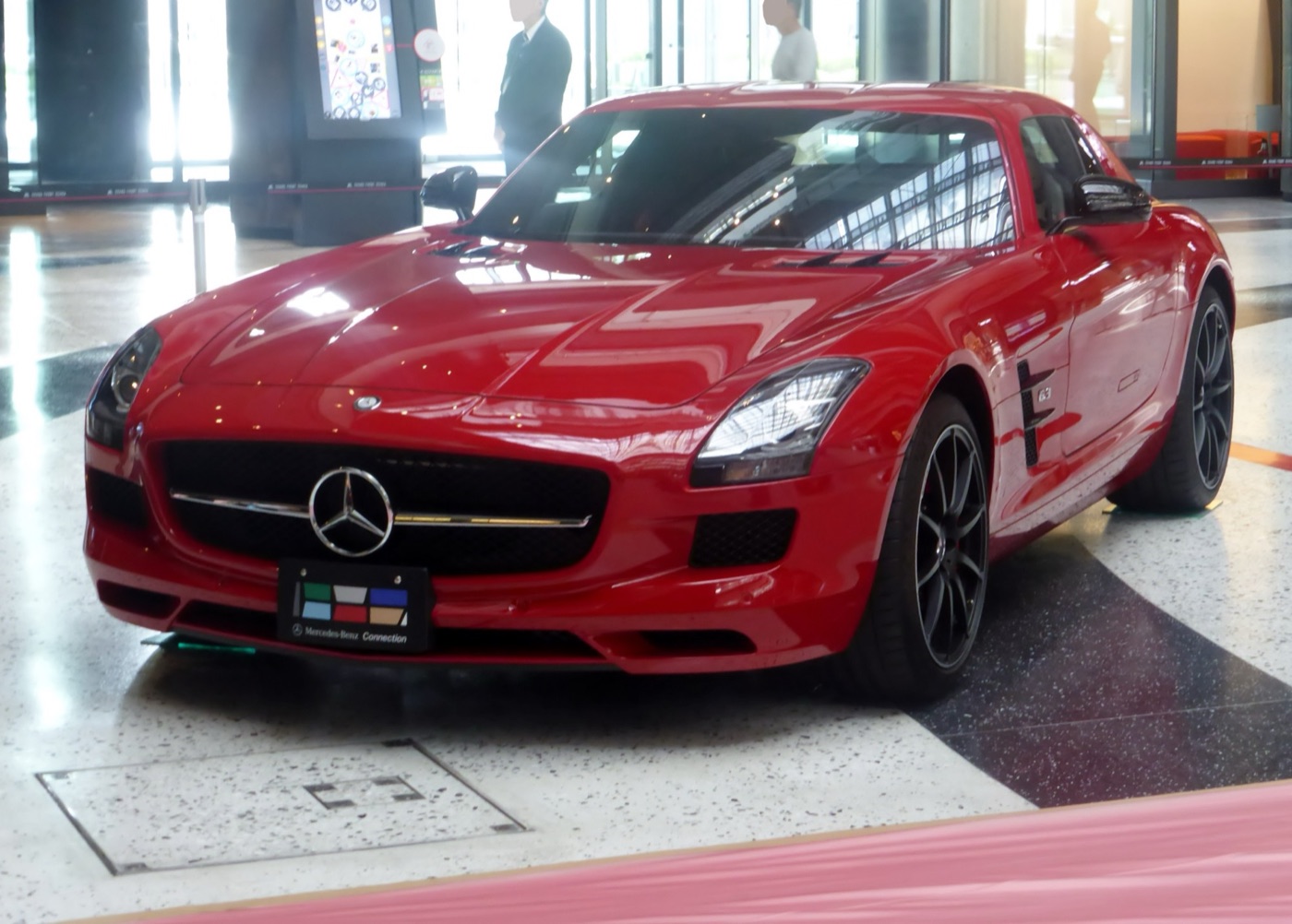 Red SLS AMG GT coupé with dark wheels and darkened headlamps parked indoors on a tiled floor