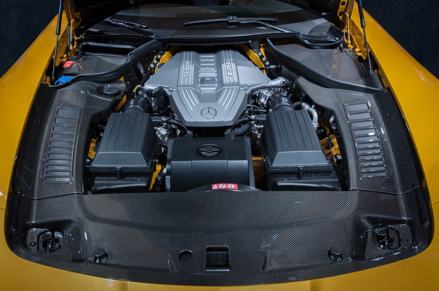 The M159 V8 engine of an SLS AMG Black Series under the open bonnet, framed by carbon-fibre panels and yellow paintwork