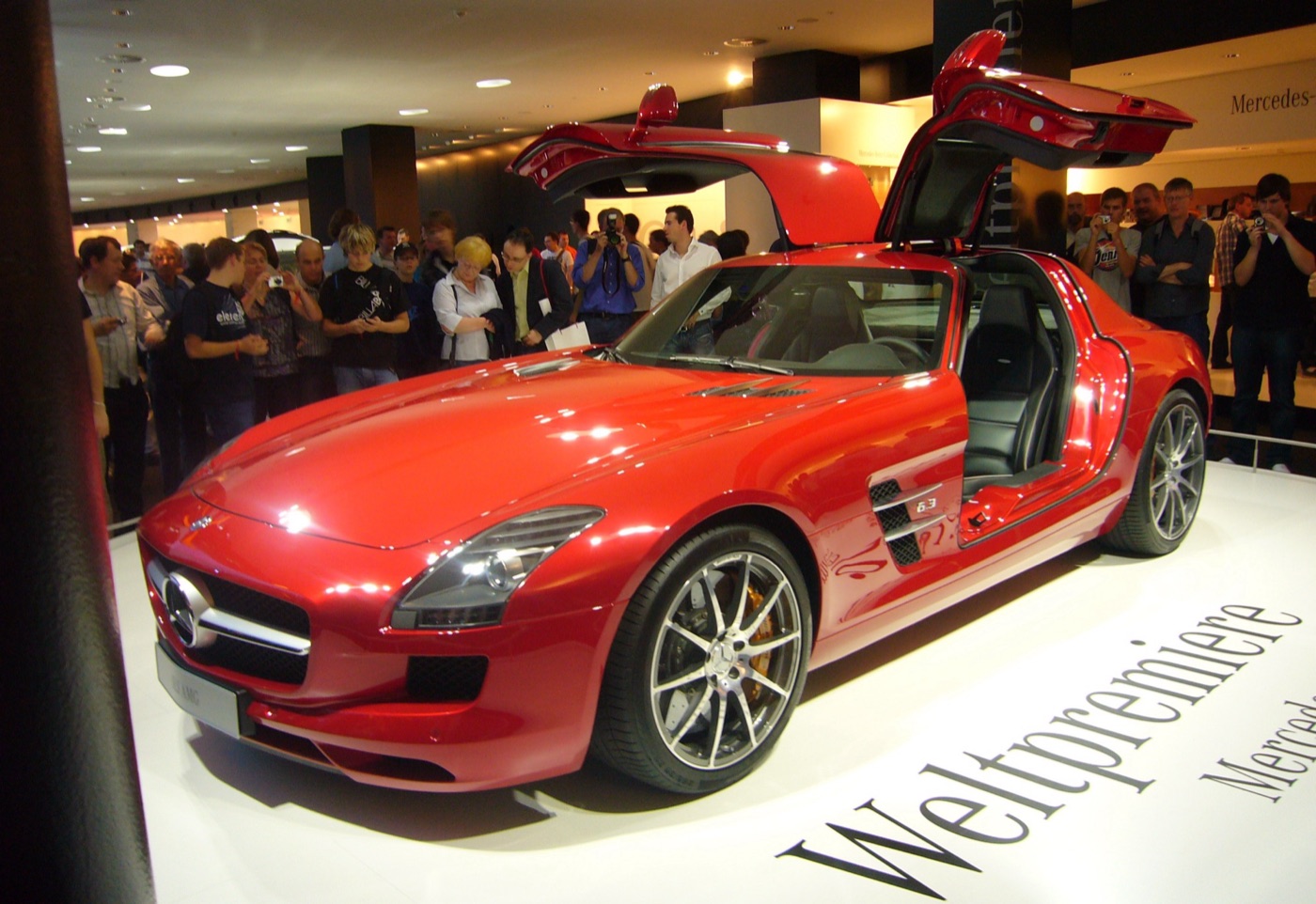 Red Mercedes SLS AMG with both gullwing doors raised on the Mercedes stand at the 2009 Frankfurt motor show, a crowd behind it
