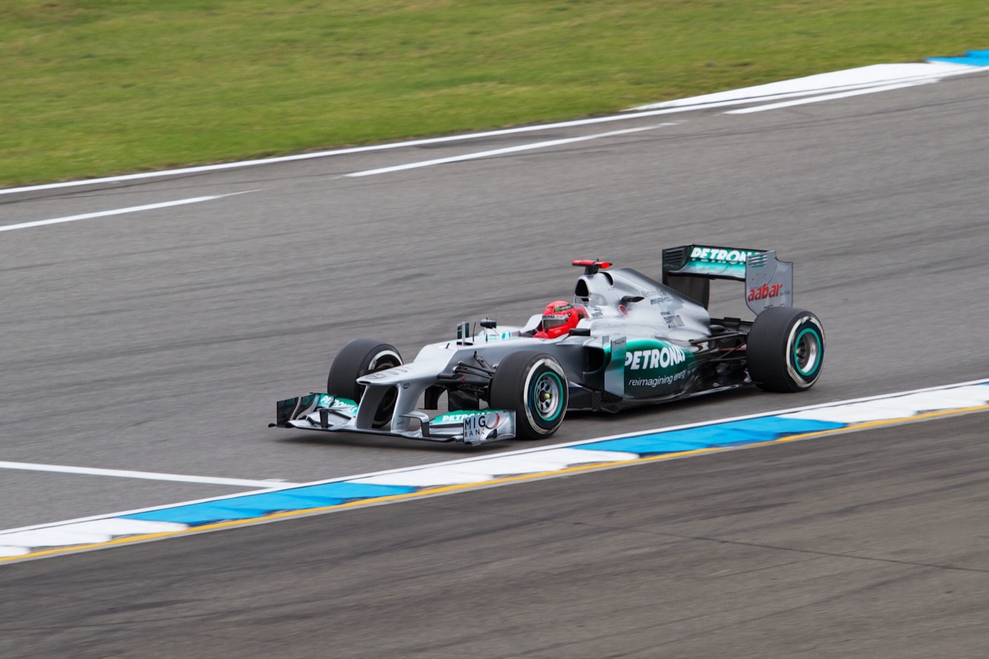 Silver and turquoise Mercedes Formula One car with Petronas and Aabar logos, driver in a red helmet, on track beside a blue and white kerb