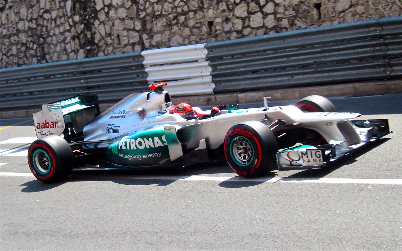 Silver Mercedes Formula One car with red-walled Pirelli tyres passing a stone wall and steel barriers on a street circuit
