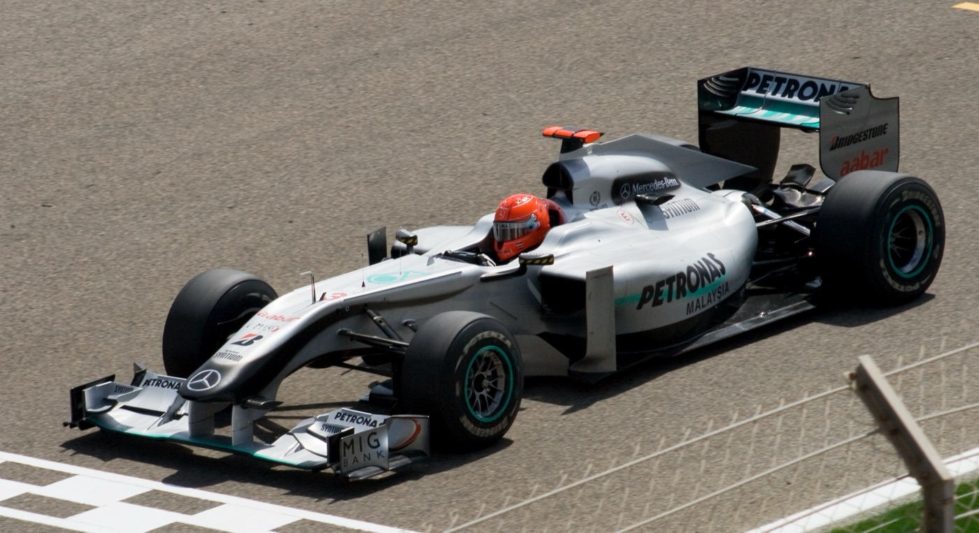 Silver Mercedes MGP W01 Formula One car with Petronas and MIG Bank logos, driver in a red helmet, crossing a chequered line on the track