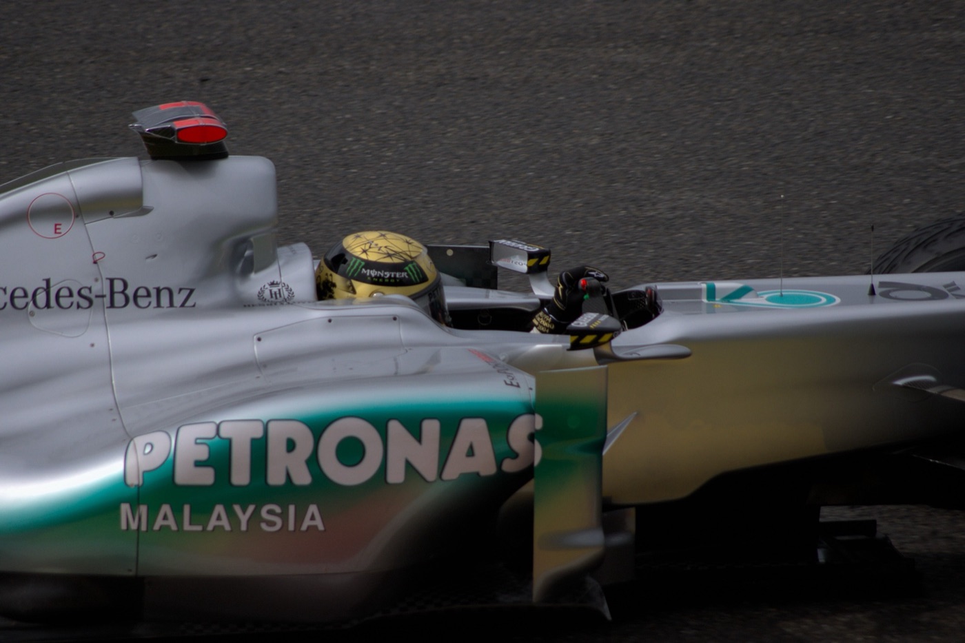 Close side view of a silver Mercedes Formula One car with Petronas Malaysia lettering, the driver in a gold helmet