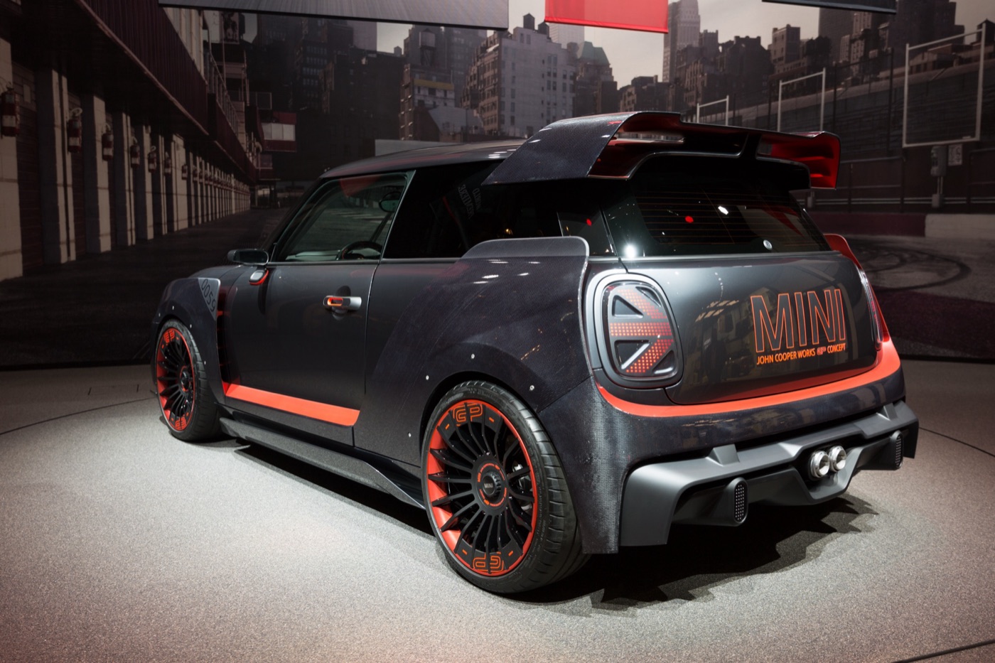 Dark MINI John Cooper Works GP Concept with orange accents, wide wheel arches and a large twin-plane roof spoiler on a motor show stand