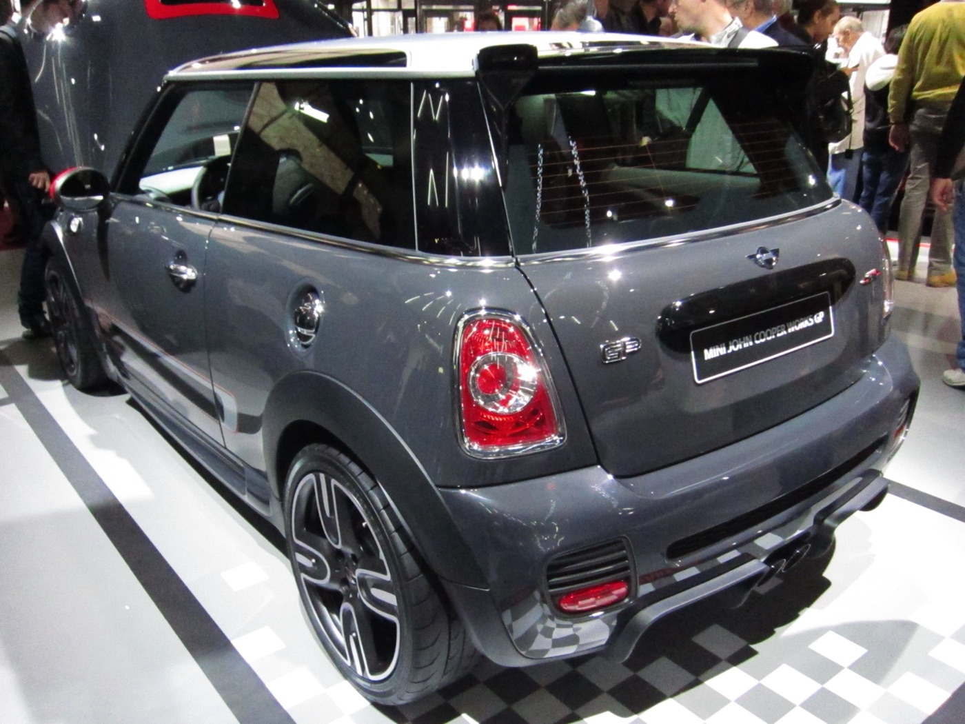 Rear three-quarter view of a grey 2012 MINI John Cooper Works GP with its roof spoiler, rear diffuser and central twin exhaust on a show stand