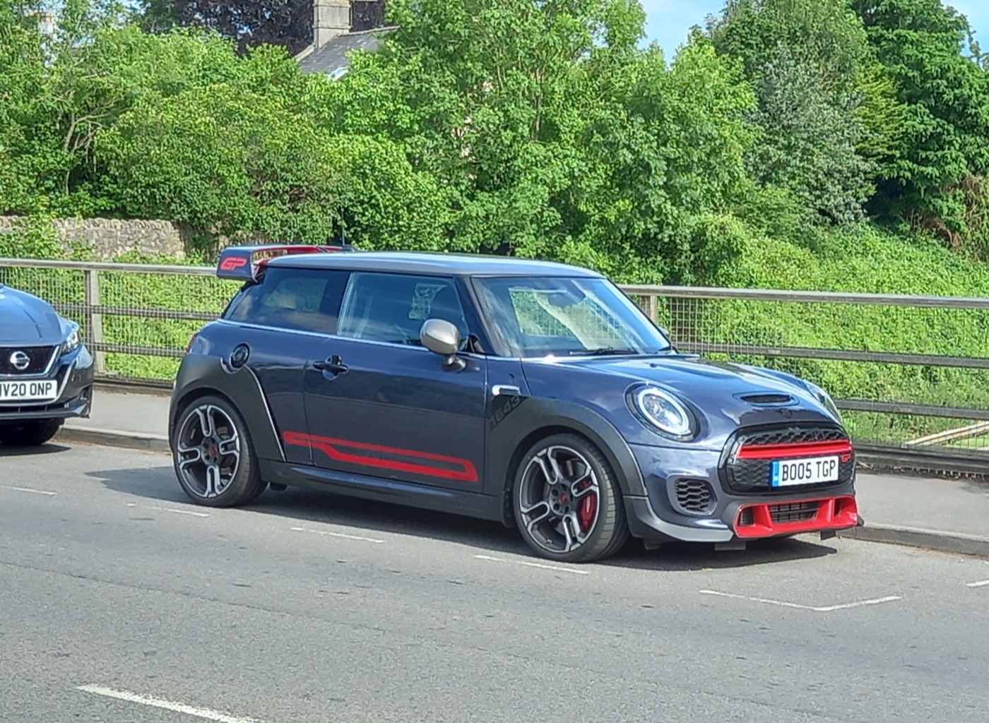 Racing Grey MINI John Cooper Works GP with red stripes, red grille trim and silver roof parked at the kerb of a road beside trees