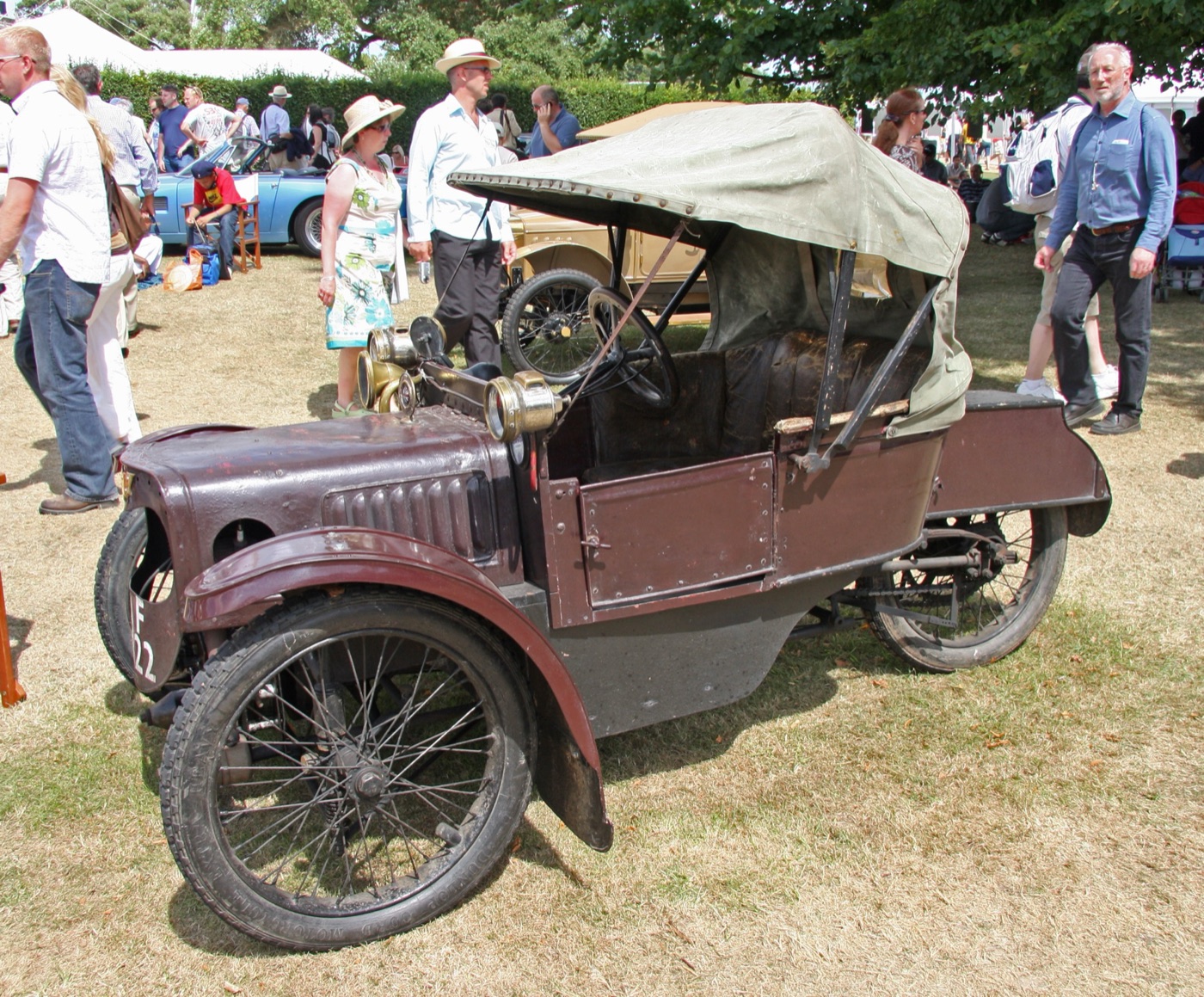 Maroon 1912 Morgan Runabout De Luxe three-wheeler with a khaki hood, wire wheels and brass lamps, parked on grass at Goodwood