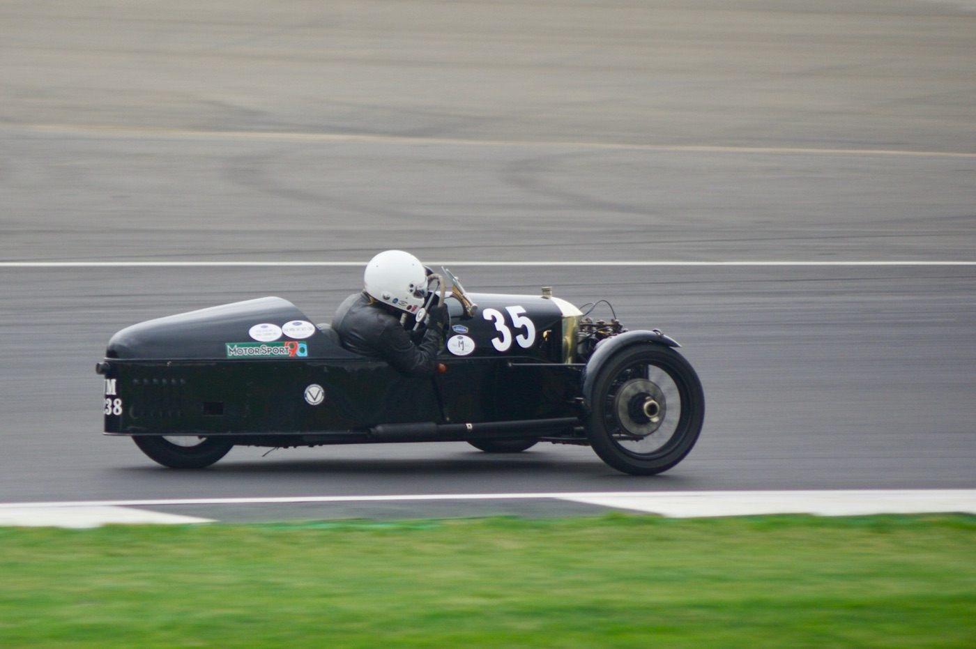 Black 1929 Morgan Super Aero racing three-wheeler, number 35, at speed on the track with its driver in a white helmet