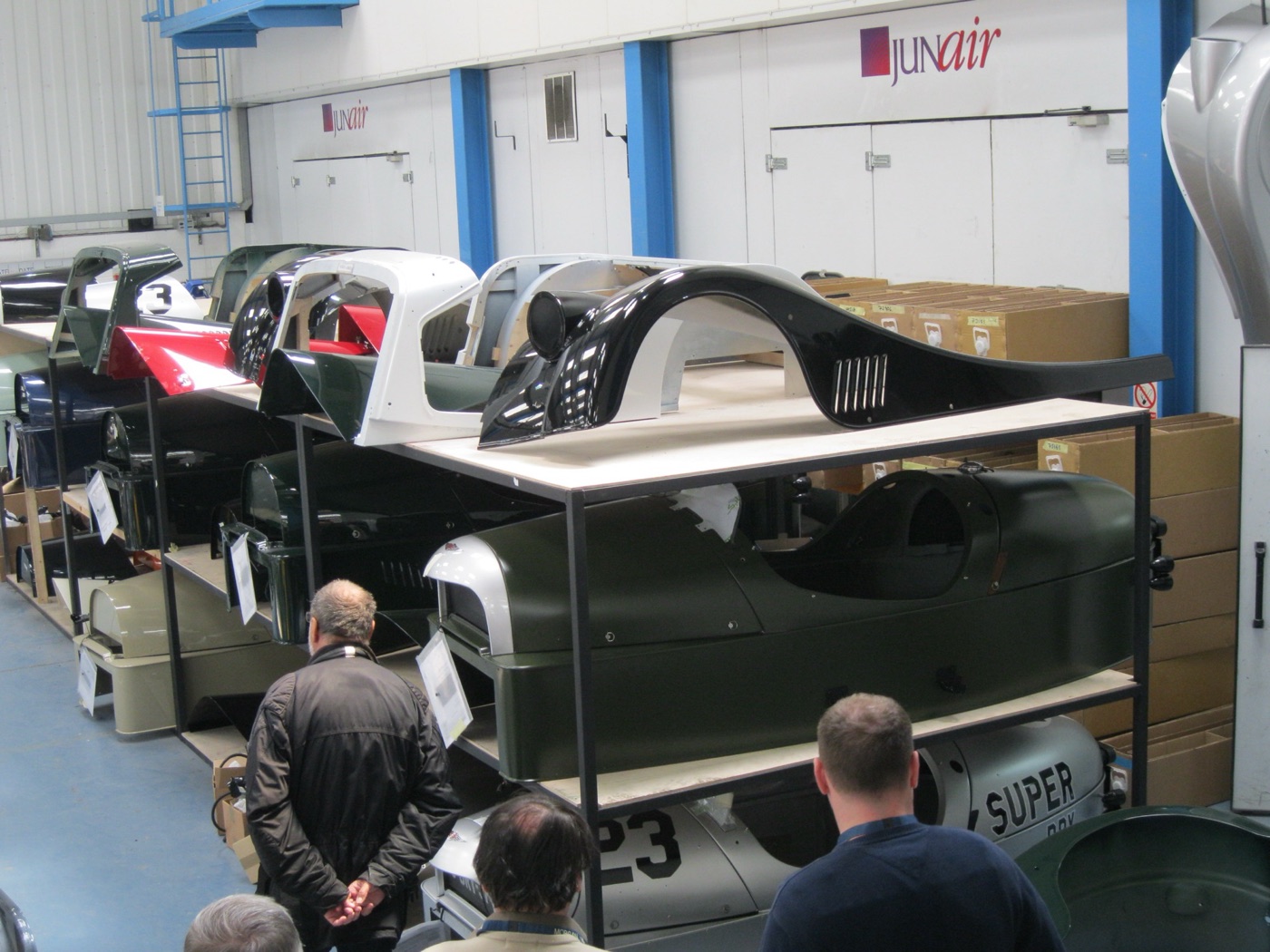 Racks of painted Morgan 3 Wheeler aluminium body tubs in several colours inside the Malvern factory, with visitors looking on