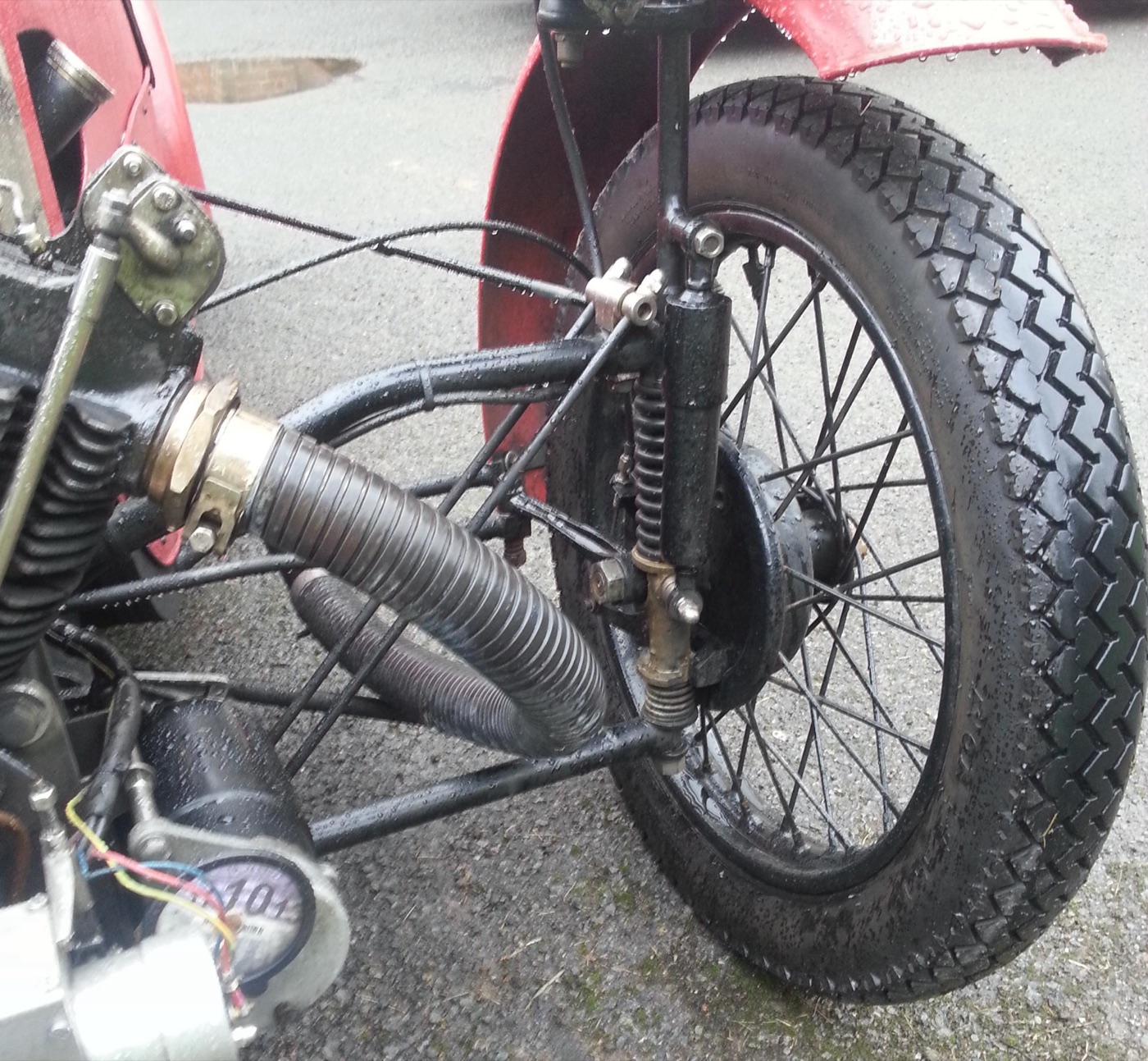 Close-up of the sliding-pillar front suspension on a 1927 Morgan three-wheeler: a vertical pillar with a coil spring, the spoked front wheel and its brake drum