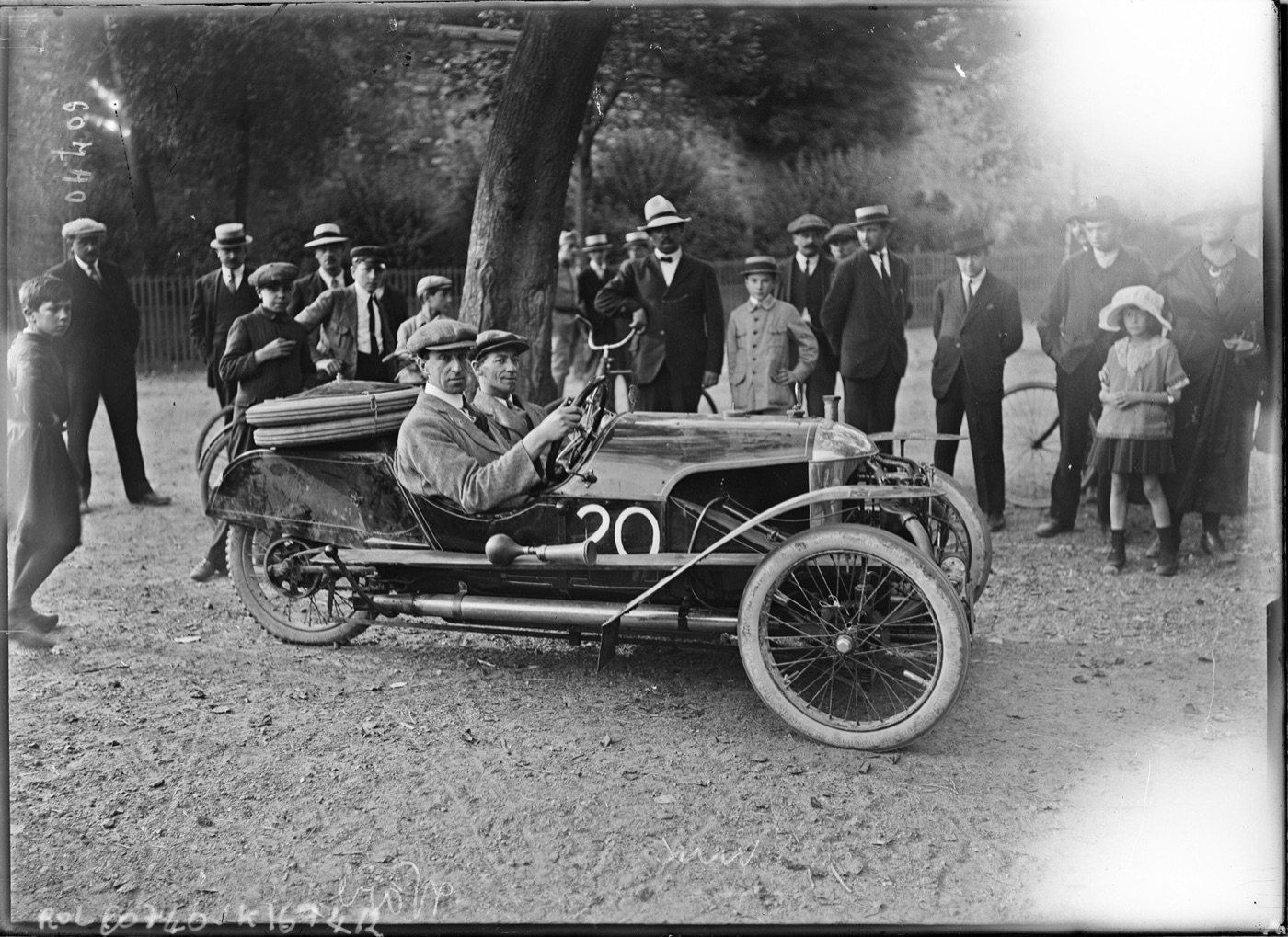 Black and white 1920 photograph of E. B. Ware seated in a Morgan three-wheeler racing car numbered 20, watched by a crowd under trees