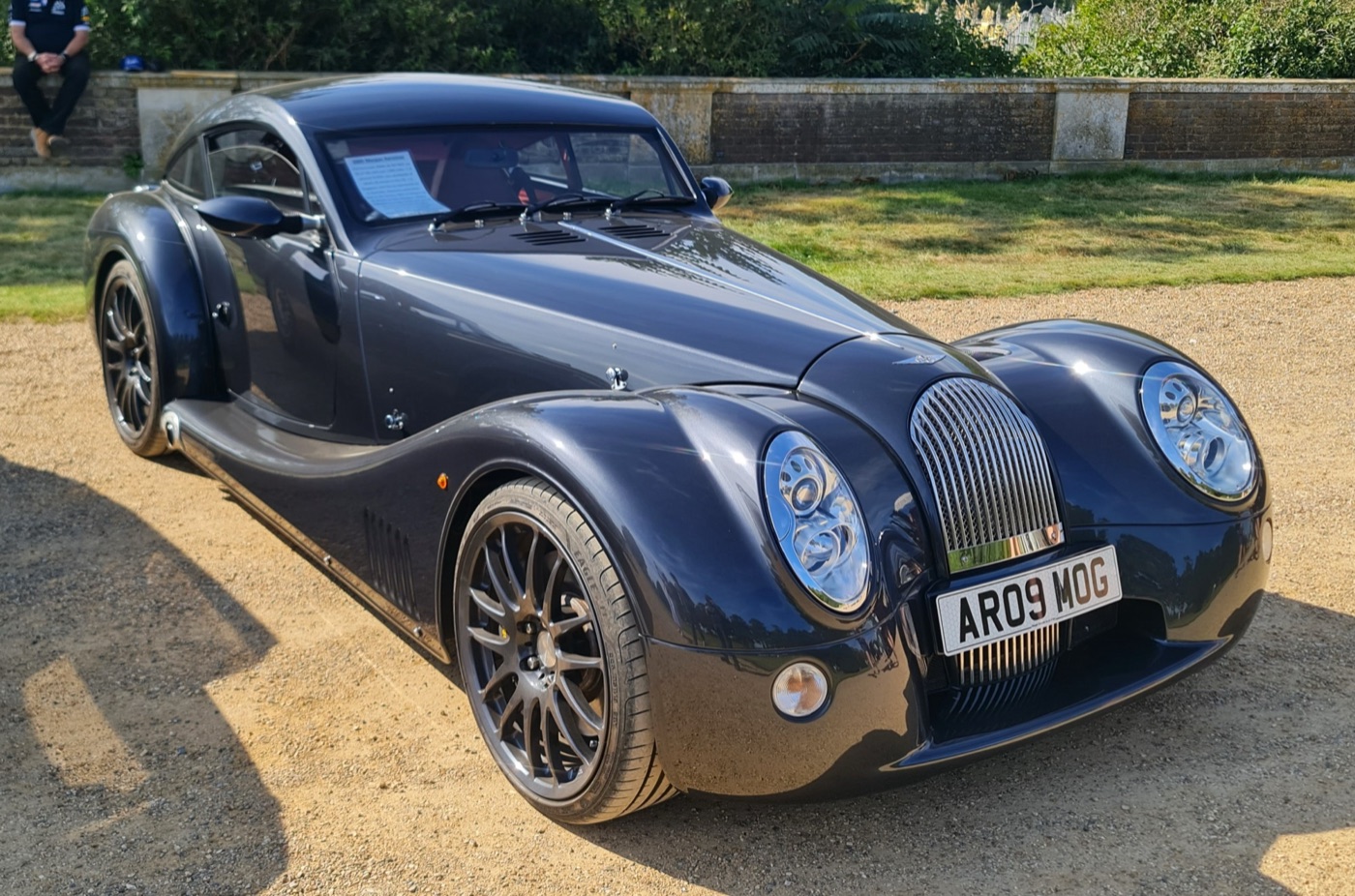 Dark grey Morgan AeroMax coupé parked on gravel at the Hampton Court Concours, seen from the front three-quarters