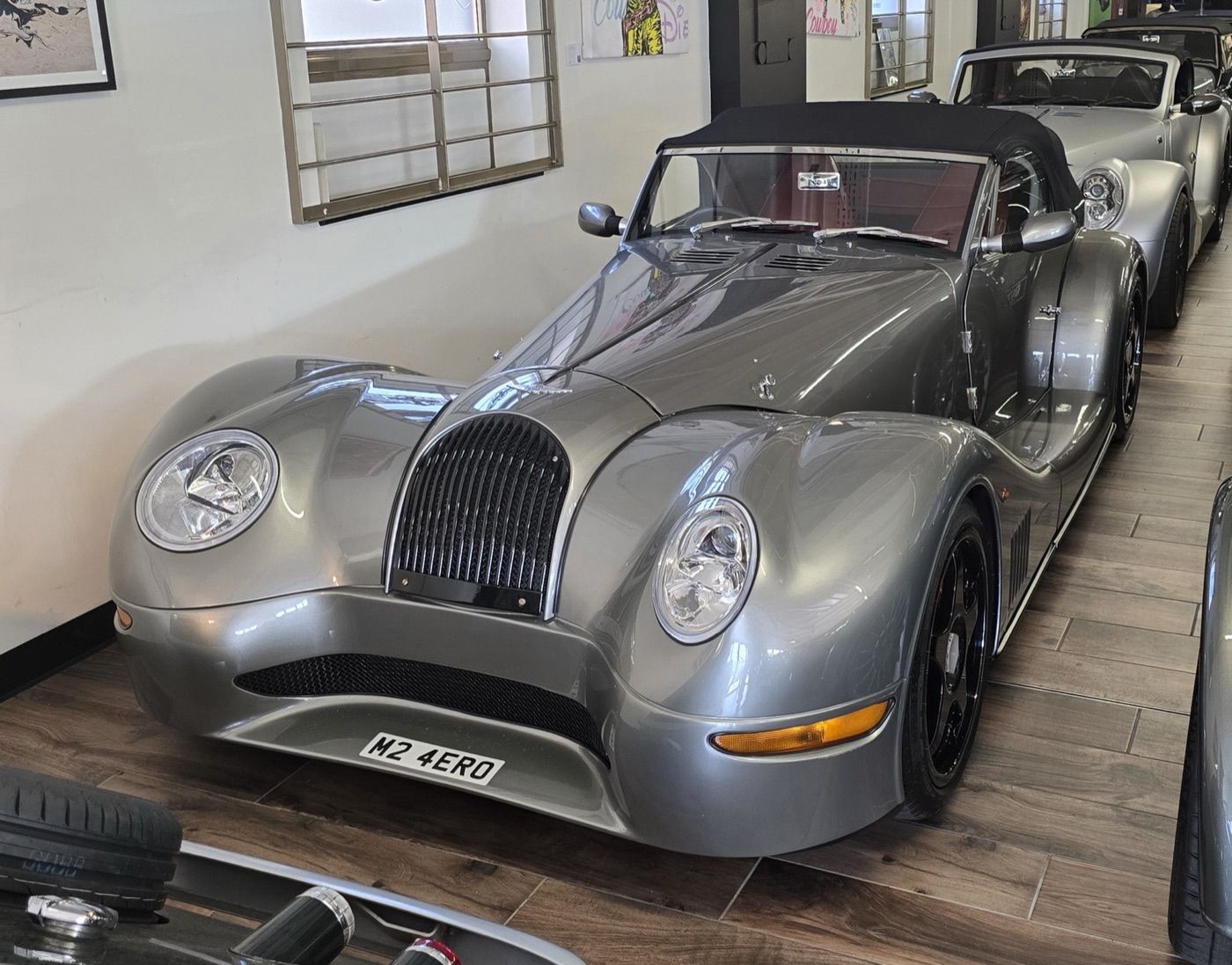 Silver 2002 Morgan Aero 8 roadster with its black hood up, cross-eyed headlamps and a black grille, parked indoors