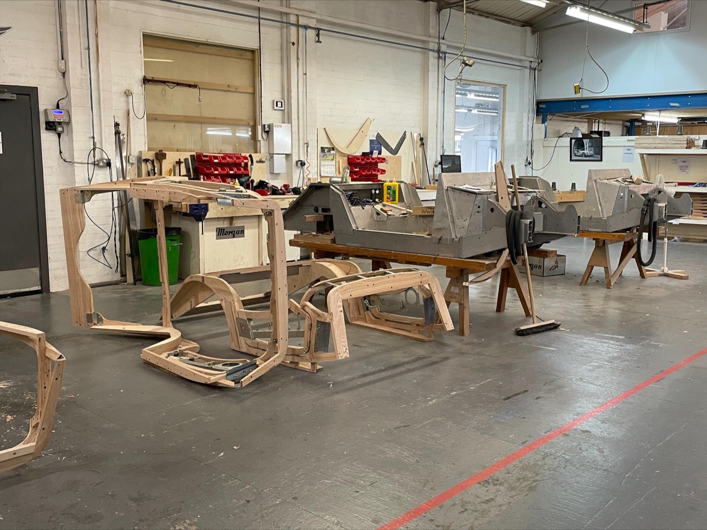 Pale ash-wood Morgan body frames and aluminium chassis tubs on trestles in the wood shop at the Malvern factory