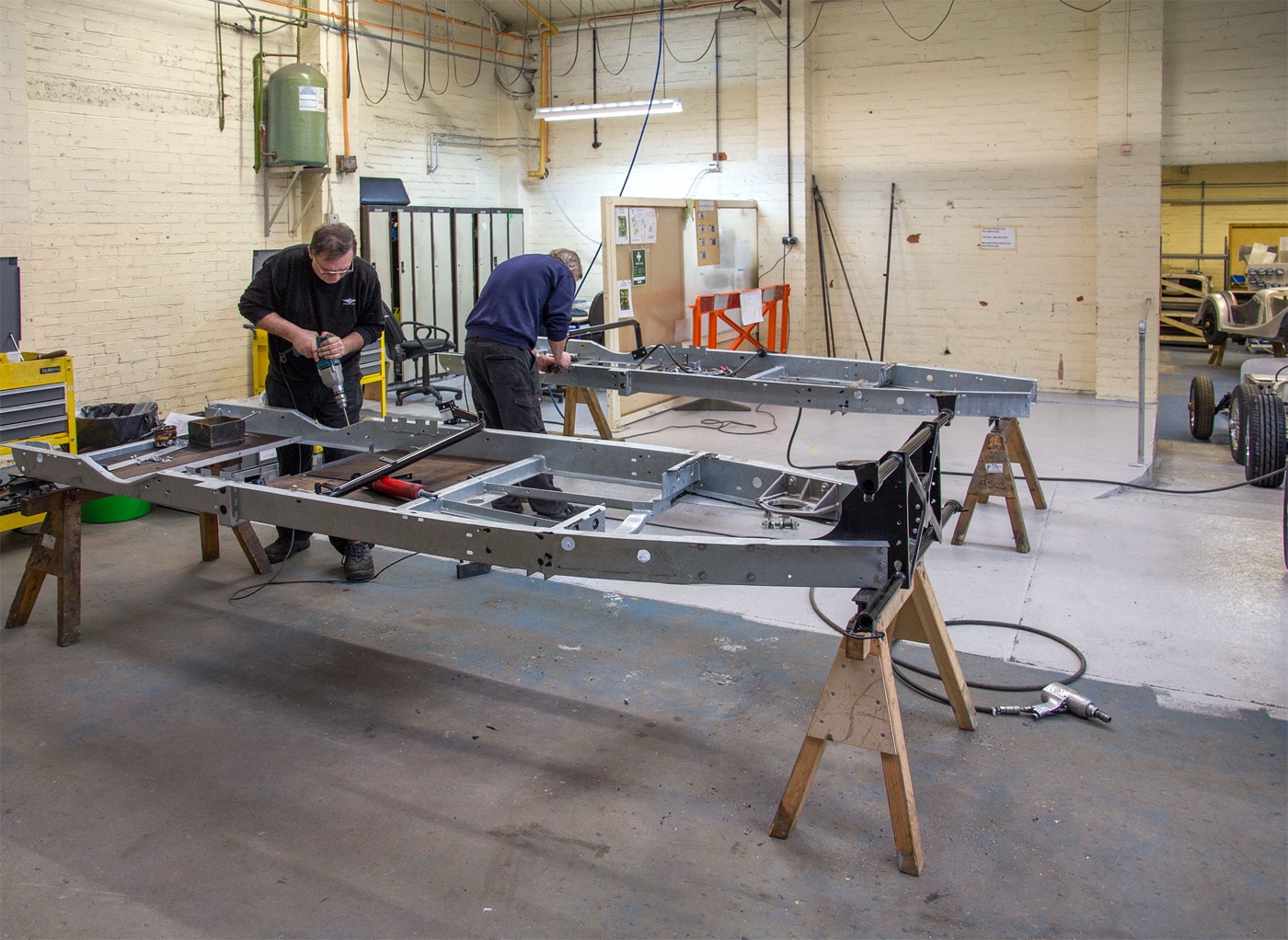 Two galvanised steel Morgan ladder chassis on wooden trestles being assembled in a whitewashed workshop