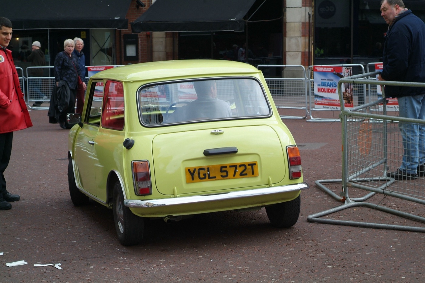 Rear of a yellow Mini with the number plate YGL 572T inside crowd barriers, with Mr. Bean