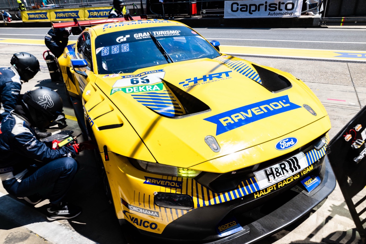 Yellow Ford Mustang GT3 number 65 in the pit lane, with crew in helmets crouched at the front wheel