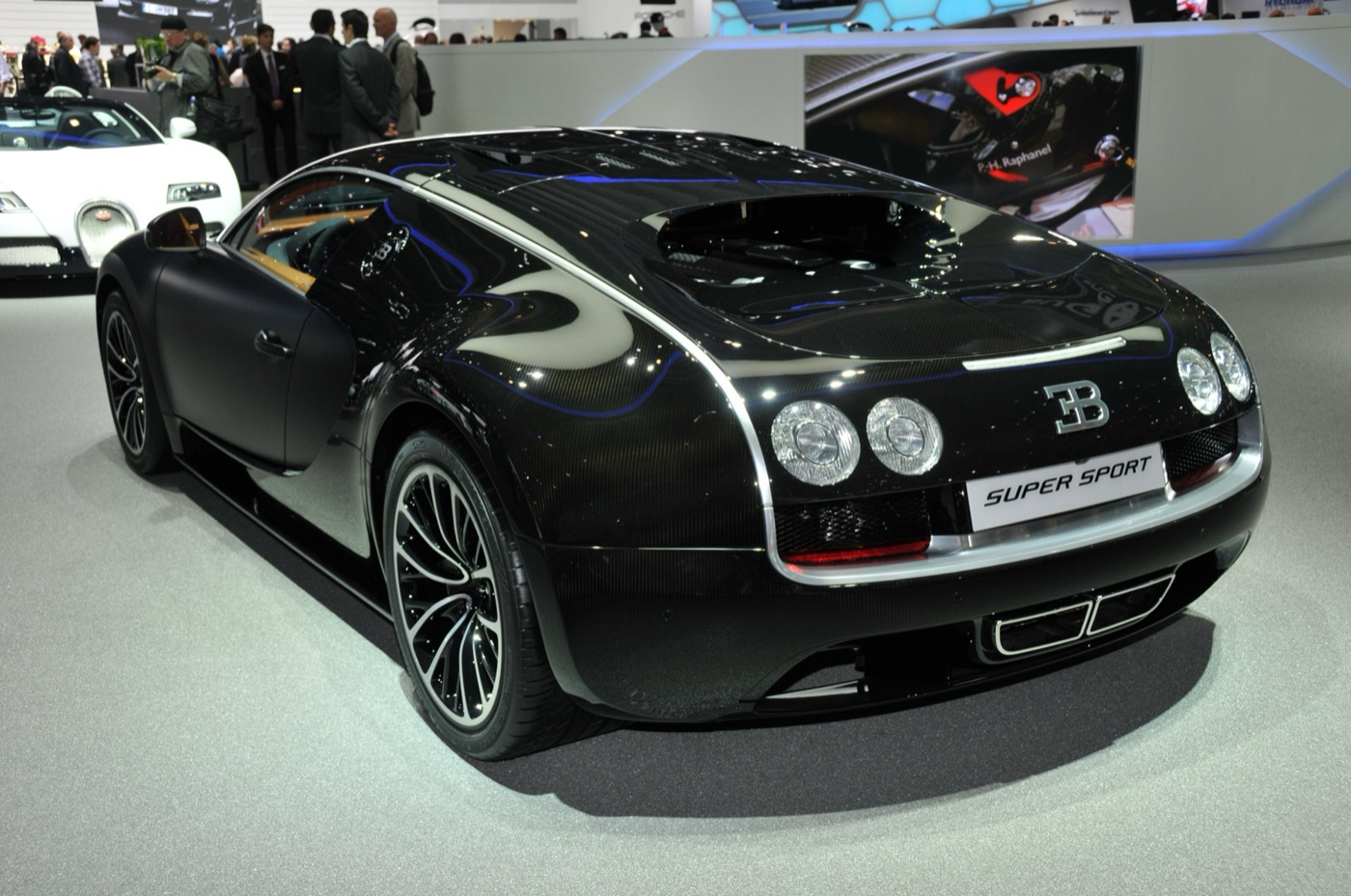 Black carbon Bugatti Veyron Super Sport seen from the rear three-quarter, with a Super Sport badge on its number plate, on a motor show stand