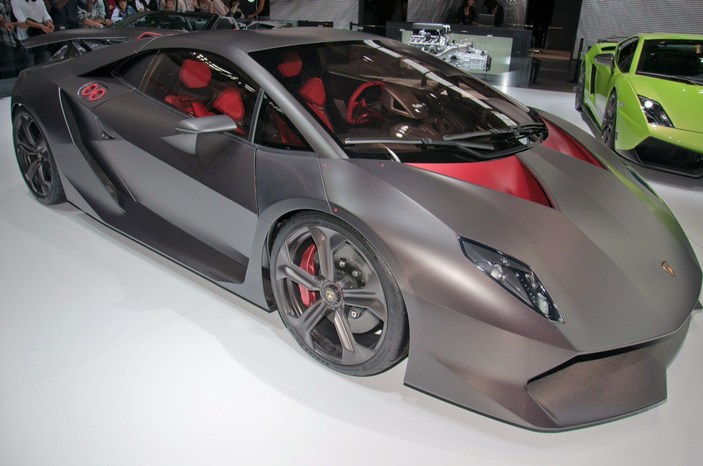 Grey carbon-fibre Lamborghini Sesto Elemento with red seats, on a white show stand with a green Gallardo behind