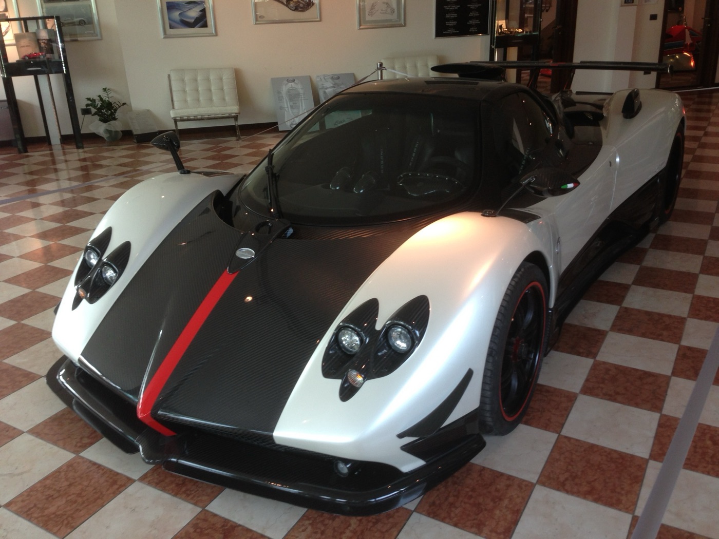 White Pagani Zonda Cinque with a black carbon bonnet and a red stripe, parked on a chequered tiled floor in a showroom