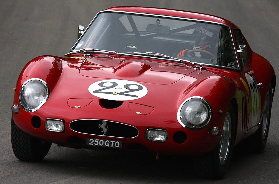 Red Ferrari 250 GTO with a yellow stripe, number 22 roundel and 250 GTO number plate, cornering towards the camera with a driver in a helmet