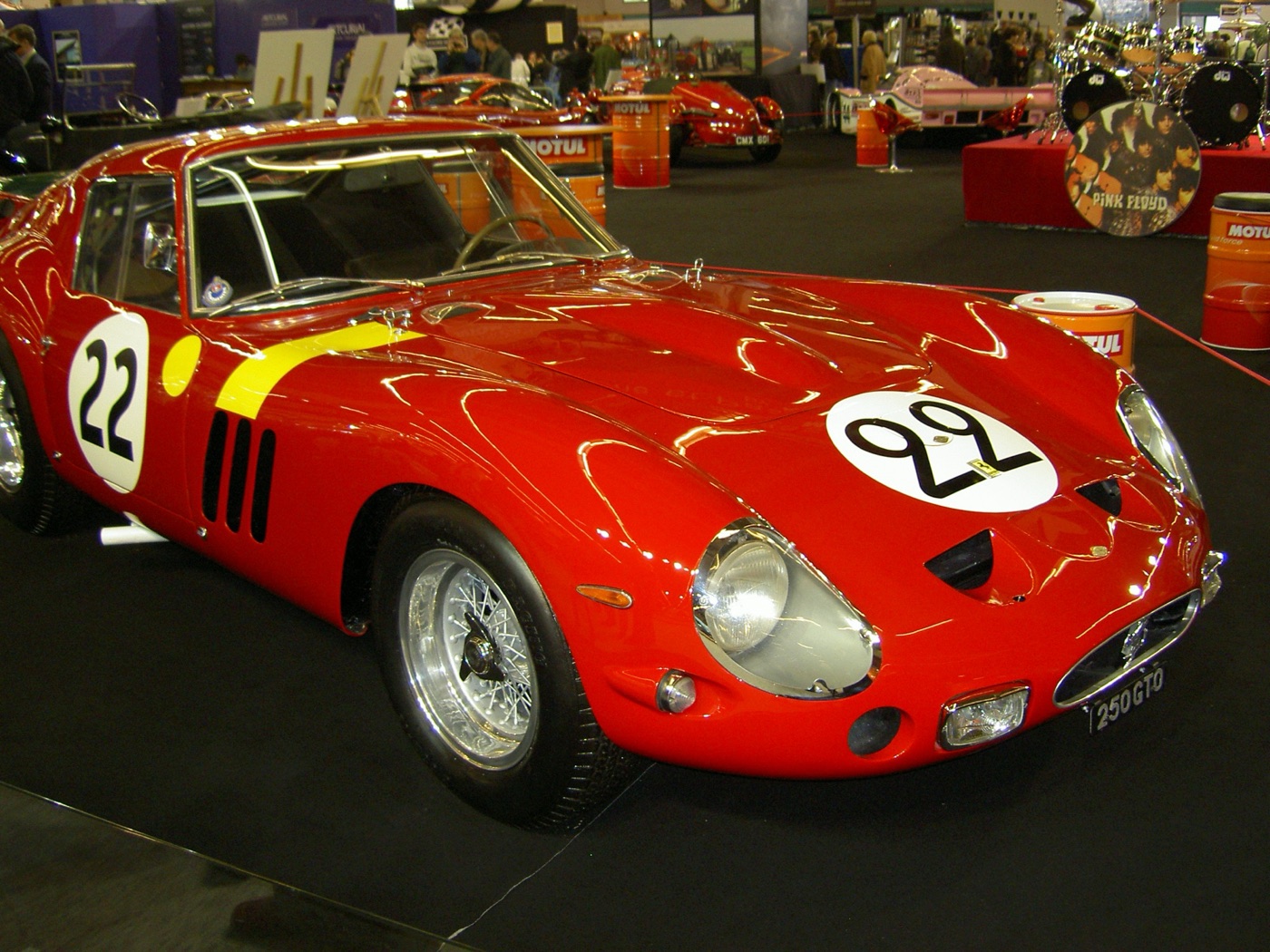 Red Ferrari 250 GTO, registration 250 GTO, with number 22 roundels and a yellow stripe, on show indoors with a Pink Floyd bass drum behind it